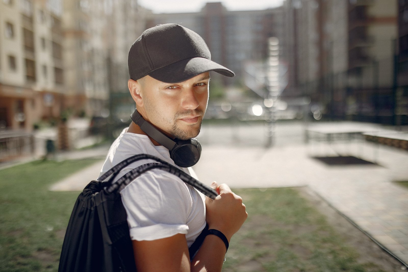 Man with a headphones. Guy in a sports clothes. Male in a summer park with backpack