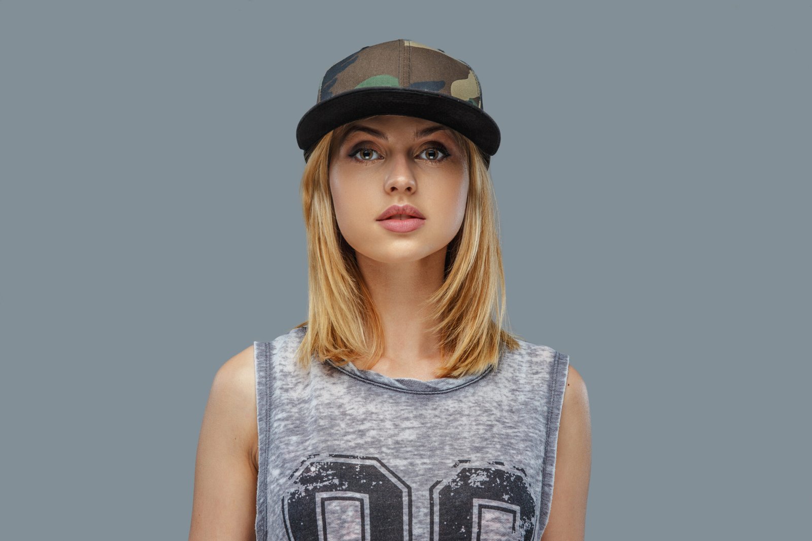 Portrait of positive blond female in baseball cap. Isolated on grey background.